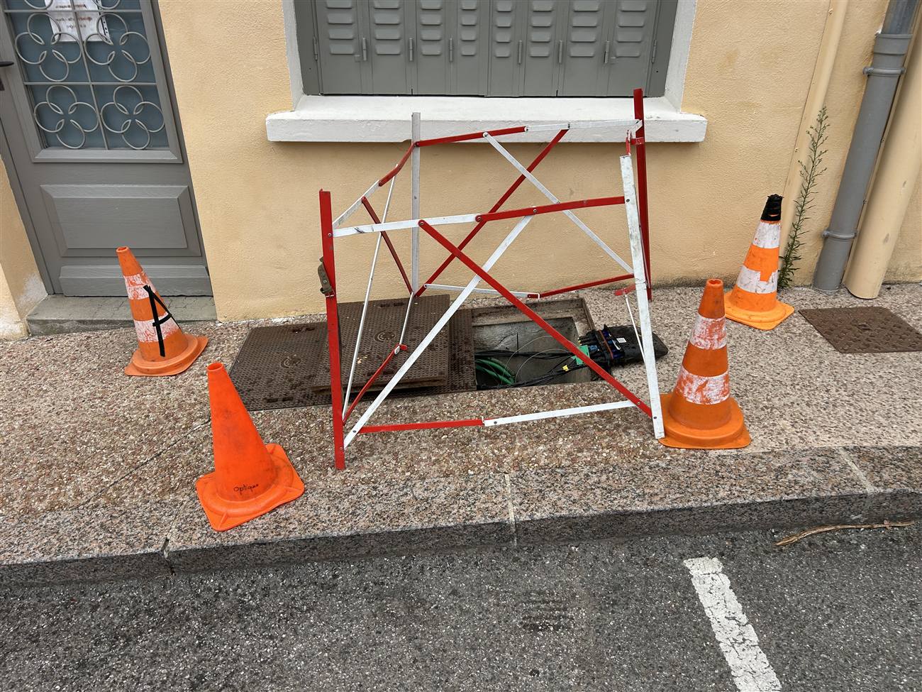 Chambre télécom ouverte en trottoir, mise en sécurité avec barrière et cônes de chantier, boîtier optique visible